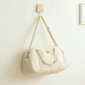Detail of embroidered bear on cream canvas diaper bag hanging on a wooden hook - White