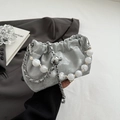 Silberne Cloud-Tasche mit Falten, Perlenkette und Metallkette auf grauem Sakko - Silber