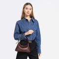 Minimalistische donkerbruine leren okseltas met slanke riem op een denim outfit - koffiekleur
