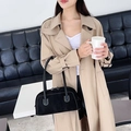 Minimalistische zwarte handtas met wit stiksel gedragen bij een beige trenchcoat - Zwart