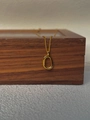 Detail einer minimalistischen Goldkette mit poliertem ovalem Anhänger auf einer Holzbox - Gold