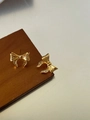 Close-up of golden bow stud earrings with delicate brushed metal texture on wood - Gold