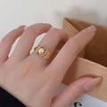 Detail of adjustable gold ring with white pearl and shell design on model hand - Gold