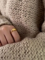 Detailed view of a gold croissant ring on finger with warm beige sweater background - Gold