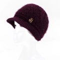 Detail eines dunkelvioletten Strickhutes mit einem goldenen apfelförmigen Metallemblem - Lila