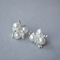 Elegante silberne Perlenohrringe mit drei weißen Perlen auf grauem Stoffhintergrund - Silber