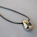 Macro shot of mirror-polished silver teardrop pendant on a black cord necklace - White Gold