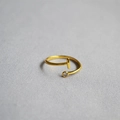 Close-up of golden T-shaped open ring with a single clear crystal on grey fabric - Alphabet Style I