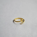 Detail of gold letter T ring with a single clear zircon on a soft grey fabric surface - Alphabet Style T
