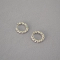 Dettaglio di orecchini a cerchio intrecciati color argento su sfondo in tessuto grigio - Argento