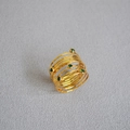 Dettaglio anello multistrato dorato con pietre preziose verdi su fondo in tessuto - US 7 / Zircone Verde