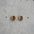 Detailaufnahme von ovalen goldenen Ohrsteckern mit violetten Cabochon-Steinen - Lila
