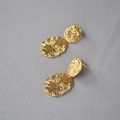 Orecchini pendenti ovali dorati con texture irregolare e raggi su tessuto grigio - Oro