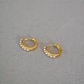 Detalle de pendientes de aro bañados en oro con seis perlas blancas sobre tela gris - Perla Artificial Huggie