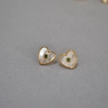 Detail van hartvormige oorbellen met wit parelmoer en een groene edelsteen centraal - Hart Groene Zirconia Oorknopjes