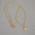 Detailaufnahme einer goldenen Stern-Halskette mit rosa Edelstein auf grauem Strukturstoff - Kette & Roter Zirkon Stern