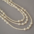Dettaglio di una collana di perle multistrato con perle di varie dimensioni su sfondo grigio - Bianco Sporco