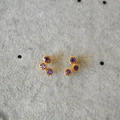 Dettaglio macro di orecchini dorati con tre pietre di zircone viola dal taglio tondo - Viola