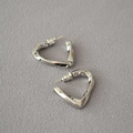 Primo piano di orecchini a forma di cuore intrecciato in argento su tessuto - Oro Bianco