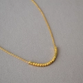 Primo piano della collana minimalista in ottone placcato oro con piccole perle a cubo - Doratura