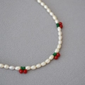 Collier de perles fait main avec breloques cerises rouges sur fond de tissu gris texturé - Trois Cerises