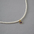 Detail einer hochglänzenden weißen Perlenkette mit rundem lila Zirkon-Anhänger in Goldfassung - Lila
