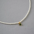 Close-up of pearl necklace featuring a green round gemstone pendant in a gold bezel - Green