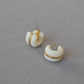 Detail of white C-shaped hoop earrings with a gold metal band on a gray fabric base - White