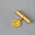 Detail of vintage gold coin pendant on a textured metal bar brooch over grey fabric - Queen