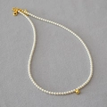 Elegante collana di perle con una sfera dorata lucida su un fondo in tessuto grigio tramato - Girocollo di Perle (Grano d'Oro)