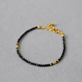 Vista macro del bracciale di perle nere sfaccettate con accenti dorati e chiusura a moschettone - Stile Spinello Nero Oro