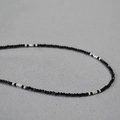Macro shot of minimalist 2mm faceted black spinel beads with silver accent beads on fabric - Black + Silver