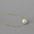 Detalle de colgante de perla de 10mm en cadena dorada sobre fondo de tela gris - Blanco Crema (12mm)