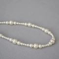 Dettaglio ravvicinato di perle color crema in dimensioni alternate su una collana elegante - Perla Artificiale Bianco Crema