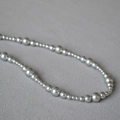 Dettaglio di collana con perle d'argento di varie dimensioni su tessuto grigio - Perla Artificiale Grigio Argento