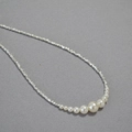 Primer plano de cadena metálica plateada irregular con perlas degradadas sobre fondo gris - Collar
