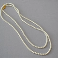 Collana di perle eleganti con chiusura a T dorata presentata su uno sfondo grigio - Stile Chiusura a Moschettone (650) / crema