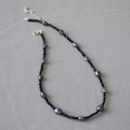 Elegante collar de espinela negra y perlas barrocas púrpuras sobre fondo de tela grisácea - Collar