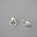 Detalle de pendientes de bola plateada pulida sobre fondo gris con textura - Plateado