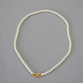 Detail of high-luster round pearls with a gold infinity-shaped clasp on a textured background - Creamy White Necklace 5mm