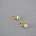 Eleganti orecchini a gancio dorati con lucide perle bianche su sfondo di tessuto grigio - Bianco Sporco 8mm