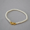 Macro detail of high-luster white pearls with a golden S-shaped infinity clasp on gray fabric - Creamy White Bracelet 4mm
