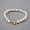 Close-up of elegant round pearls with a golden infinity clasp on a soft fabric background - Creamy White Bracelet 8mm