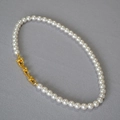 Dettaglio di elegante collana di perle con chiusura a maglia a U dorata su sfondo grigio - Stile Perla Bianco Crema Oro (8mm)