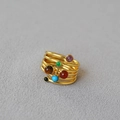 Dettaglio anello in ottone dorato multistrato con sei pietre colorate su fondo grigio - US 7