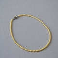 Dettaglio di elegante collana di perle dorate tonde con chiusura in metallo minimalista - 4mm