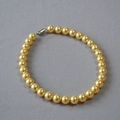 Élégant collier de perles dorées avec fermoir métallique sur fond gris - 12mm