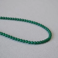 Collana di perle in agata verde stile etnico su sfondo di tessuto grigio testurizzato - 4mm