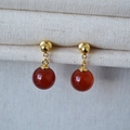 Dettaglio di orecchini pendenti dorati con perle di agata rossa su tessuto a maglia bianco - Agata Rossa da 10mm