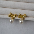 Eleganti orecchini a fiocco dorati con perle bianche su sfondo in tessuto color crema - Oro